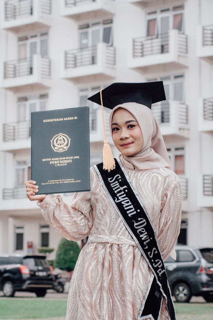 About Young Muslim woman in hijab celebrates graduation outdoors in Indonesia.