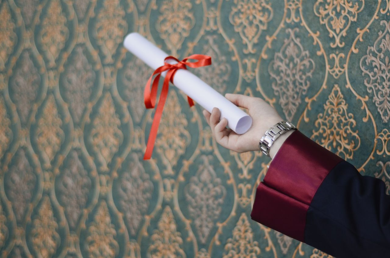 A graduate's hand holding a diploma with red ribbon, symbolizing achievement.
