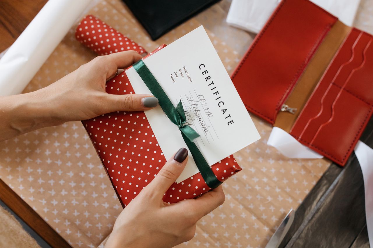 Services Close-up of hands holding a gift certificate wrapped in red polka dot paper and green ribbon.
