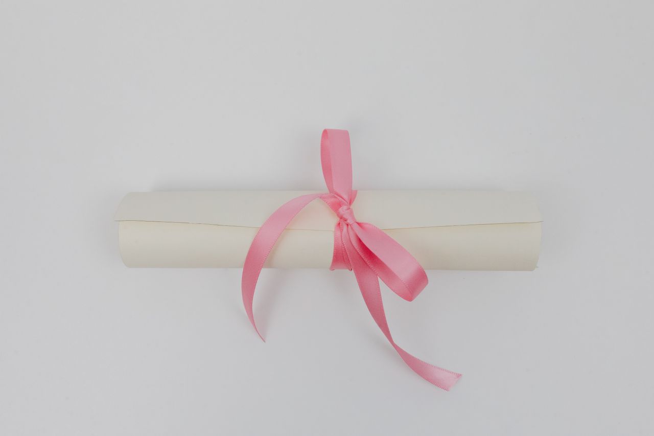 Services A minimalist top view of a rolled paper tied with a pink ribbon against a white background.
