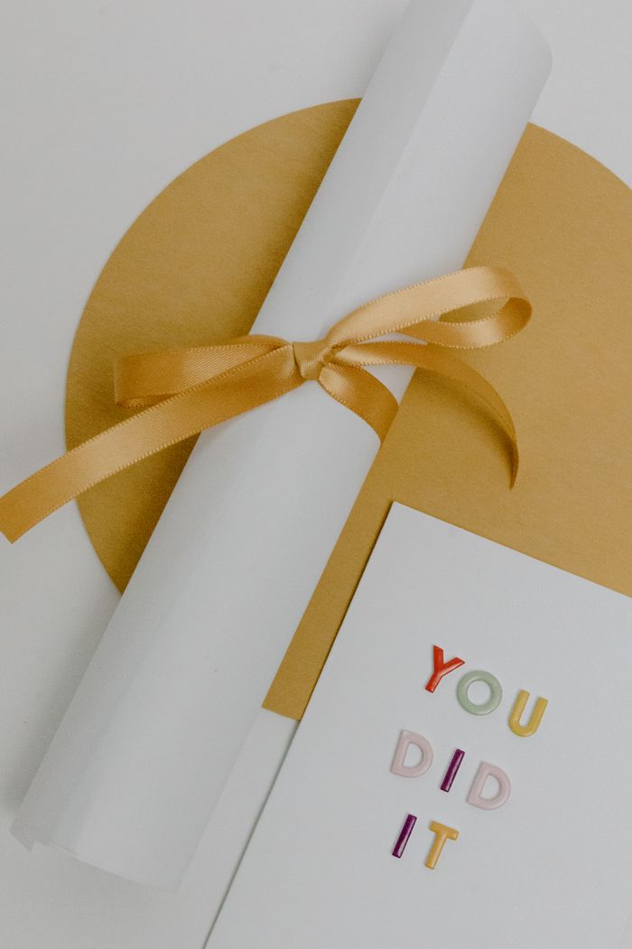 Services Rolled white certificate tied with gold ribbon on textured background next to congratulatory card.